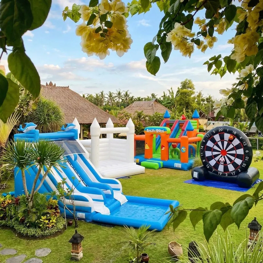 A white bouncy castle, an inflatable water slide and a giant football dart set up in a garden in Bali